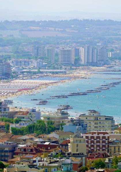 Vista panoramica di una città costiera con spiagge affollate e mare blu.