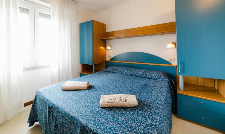 Camera d'hotel con letto matrimoniale, armadi blu e finestra luminosa.